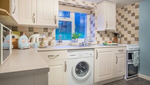 A modern kitchen with white cabinets, a built-in washing machine, a window with a view, and a tiled backsplash.
