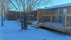 A wooden deck with a railing, a covered patio area, and a building with a window and a door. - Cedar Creek Standard 1 (East Braintree)