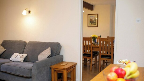 A living room with a grey sofa, a small wooden table, and a fruit bowl on a wooden table.