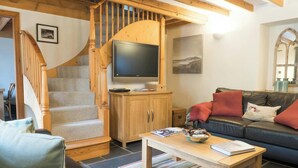 Een woonkamer met een trap, een flatscreen televisie, een bank en een salontafel.