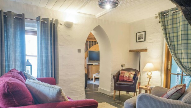 Een woonkamer met een rode bank, een grijze fauteuil, een houten tafel met een lamp en een televisie op de achtergrond.