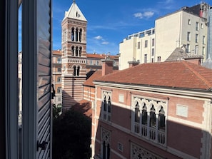 Vista de un edificio histórico con una torre destacada y ventanas en arco, rodeado de otros edificios.