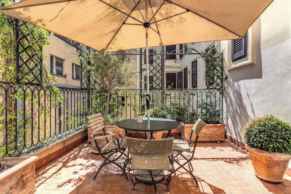 Un patio al aire libre con una mesa redonda, sillas y un gran paraguas.