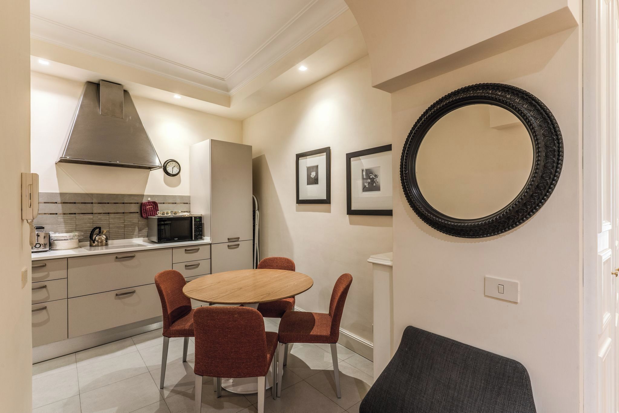 Una cocina moderna con una mesa de comedor redonda, sillas rojas, un microondas y un espejo grande en la pared.