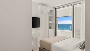 Une chambre avec un lit, une télévision, une armoire et un balcon donnant sur la mer.