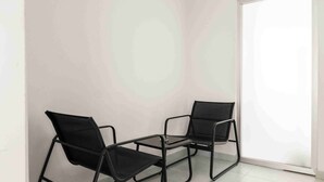 Une pièce avec deux chaises à armature métallique noire et une petite table, un mur blanc et une grande fenêtre.