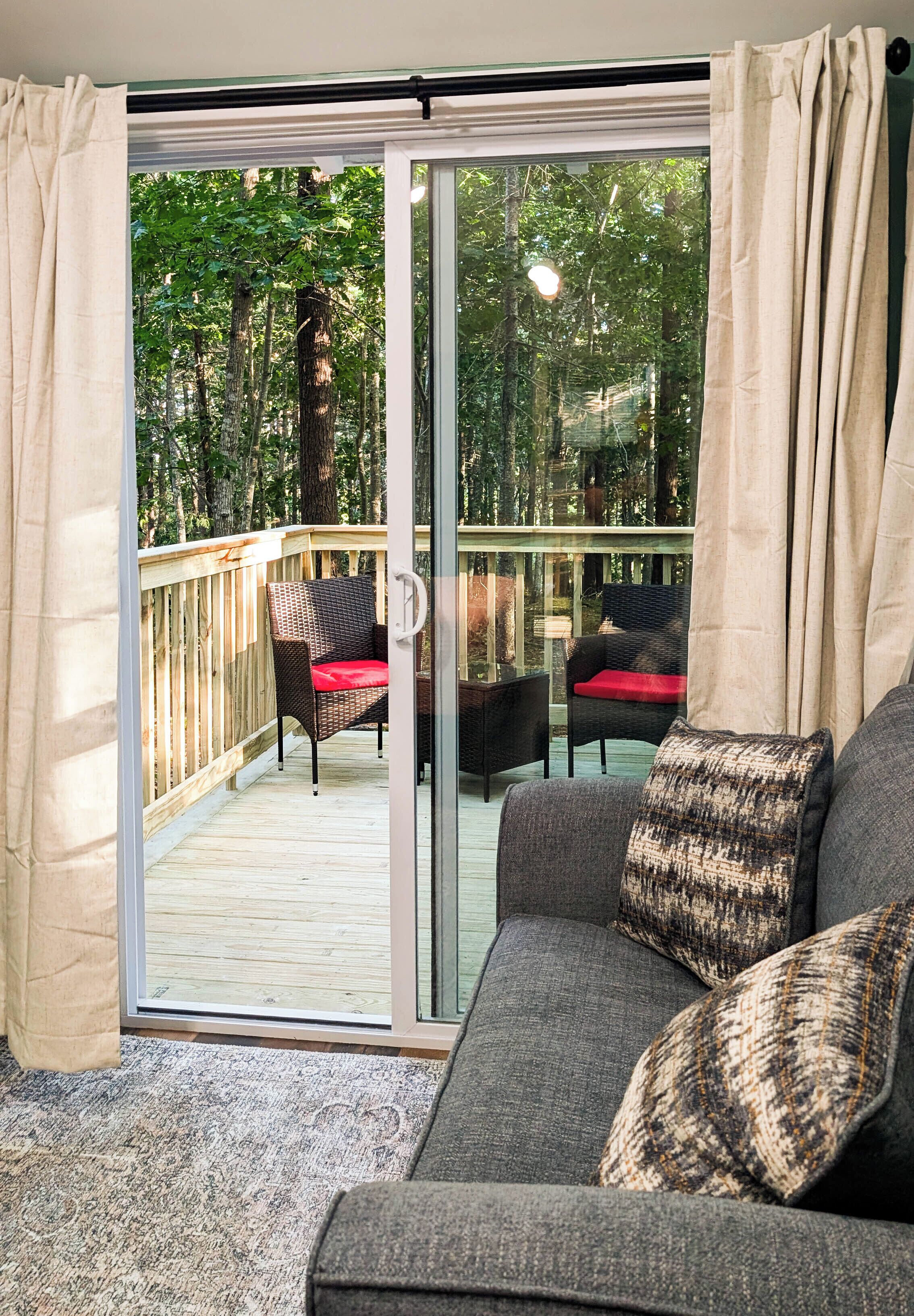 Une pièce dotée d’une porte-fenêtre coulissante qui donne sur une terrasse extérieure aménagée avec des meubles en osier et un coussin rouge.