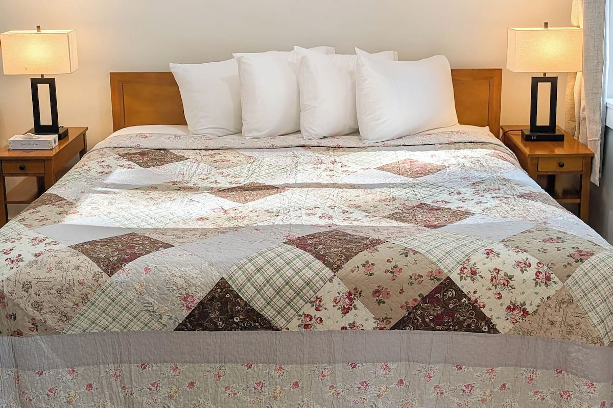 A hotel room with a large bed, two nightstands, a wall-mounted air conditioner, and two framed pictures of flower markets.