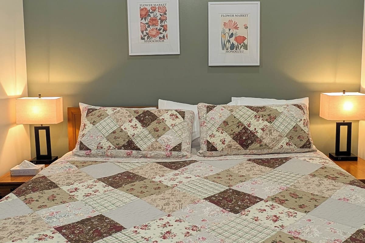 A bed with a floral quilt, two framed pictures on the wall, and two bedside lamps.