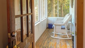 A wooden door with a "No Smoking" sign, a rocking chair, and a view of trees through a covered porch. - Hinckleys Dreamwood Cottages (Bar Harbor)
