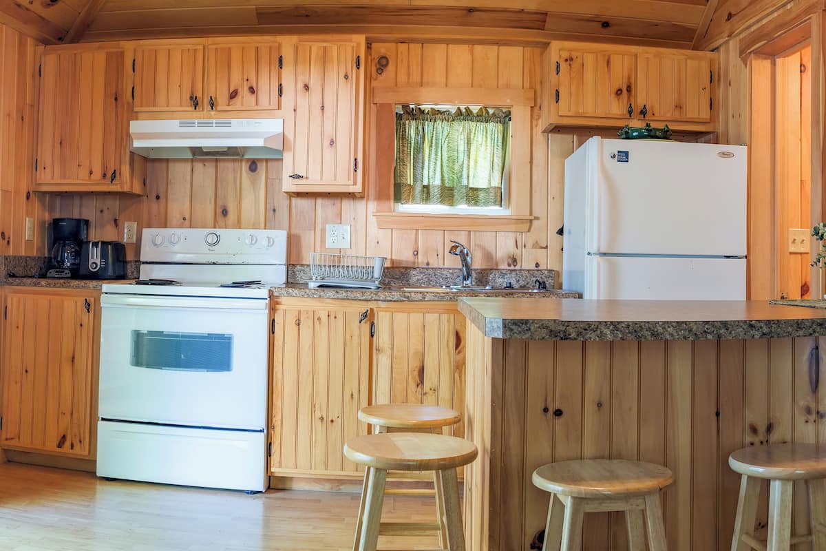 A wooden cabin kitchen with a stove, refrigerator, and bar stools.
