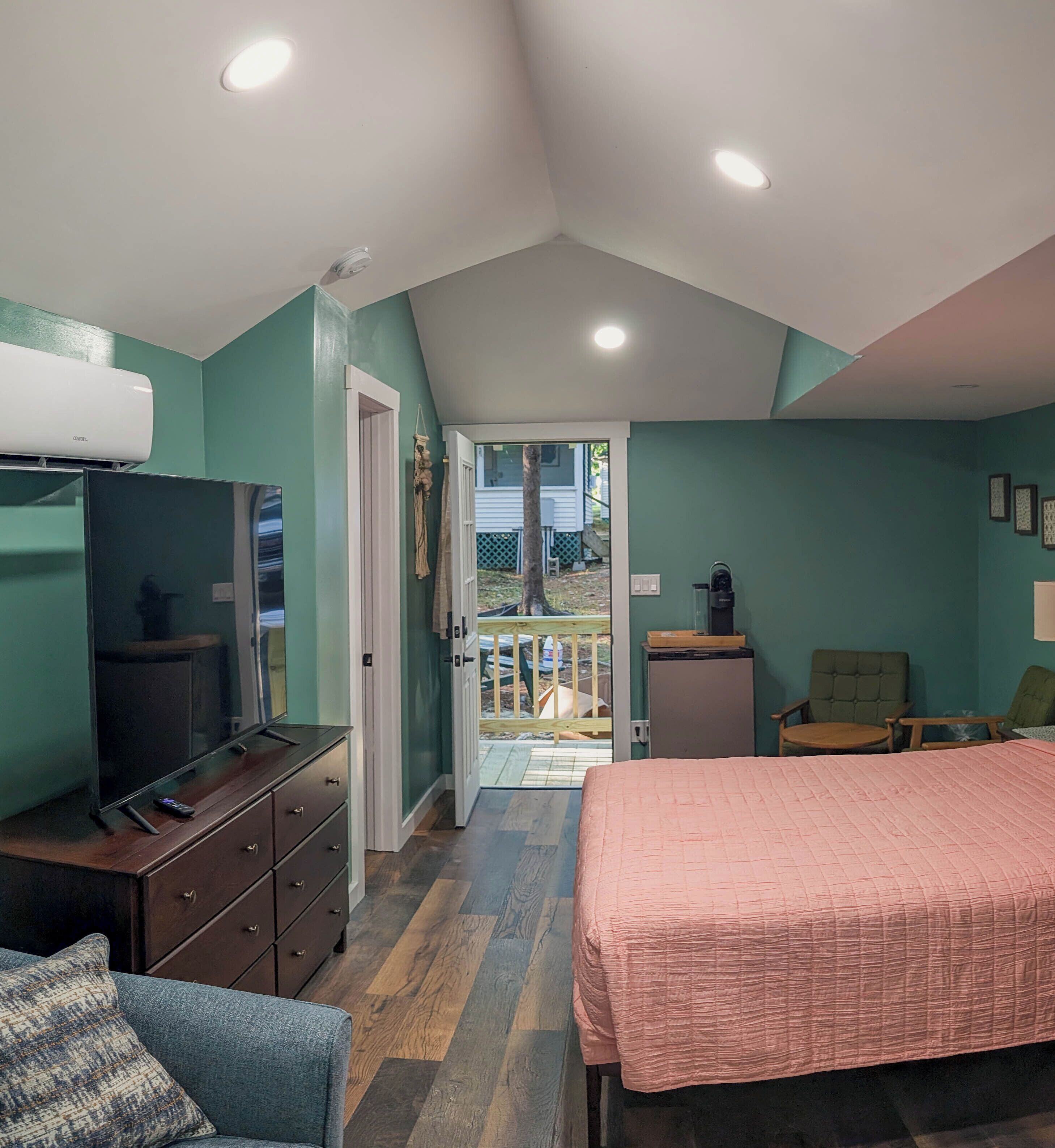A bedroom with a bed, dresser, TV, and a balcony with a view.