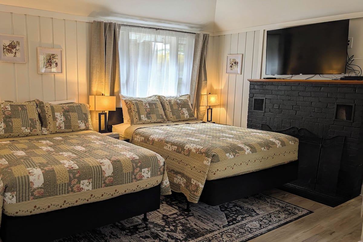 A double room with two beds, each with floral-patterned bedding, a fireplace, and framed botanical artwork on the walls.