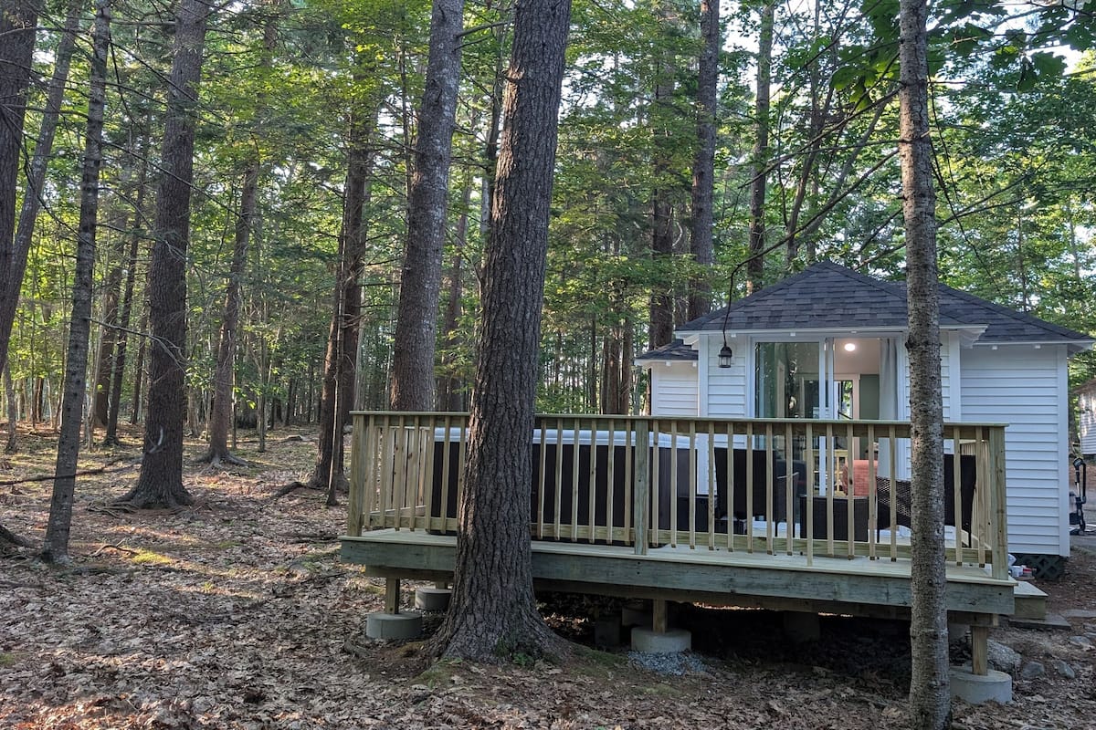A small cabin with a deck, surrounded by tall trees in a forest.