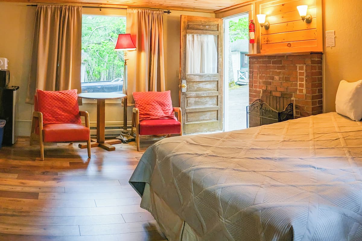 A cozy room with a bed, two chairs, a table, and a fireplace.