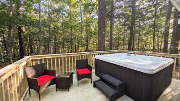 A deck with wicker chairs and a hot tub, surrounded by a forest.