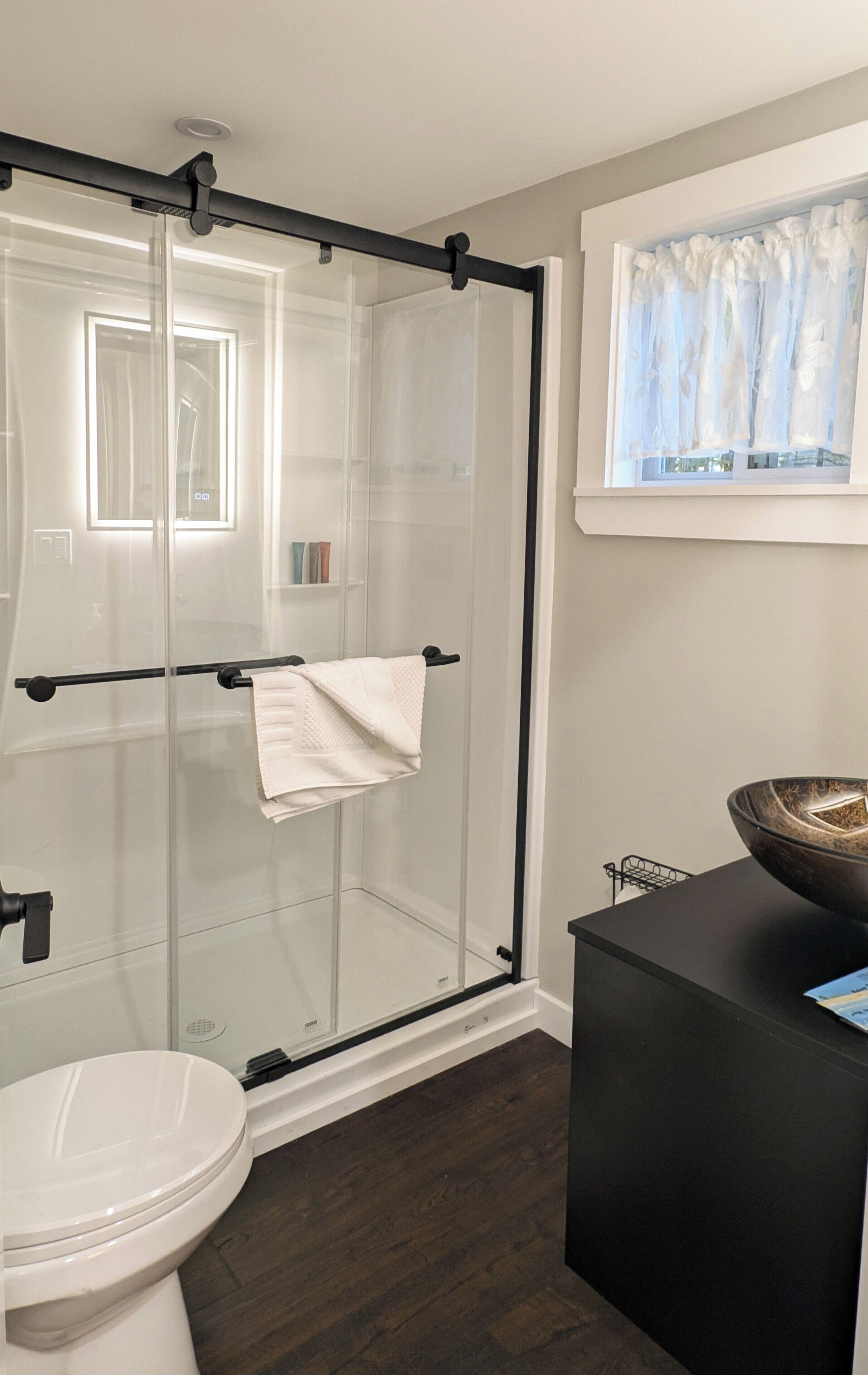 Een moderne badkamer met een douchecabine van glas, een wit toilet en een zwarte wastafel met een wasbak.
