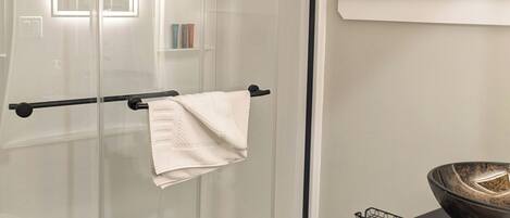 A modern bathroom with a glass shower enclosure, a white toilet, and a black vanity with a bowl.