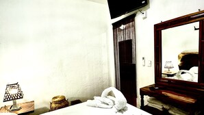 A hotel room with a bed, a TV mounted on the wall, a wooden nightstand, and a mirror.