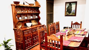 A dining area with a wooden table and chairs, a cabinet with glassware, and a potted plant.