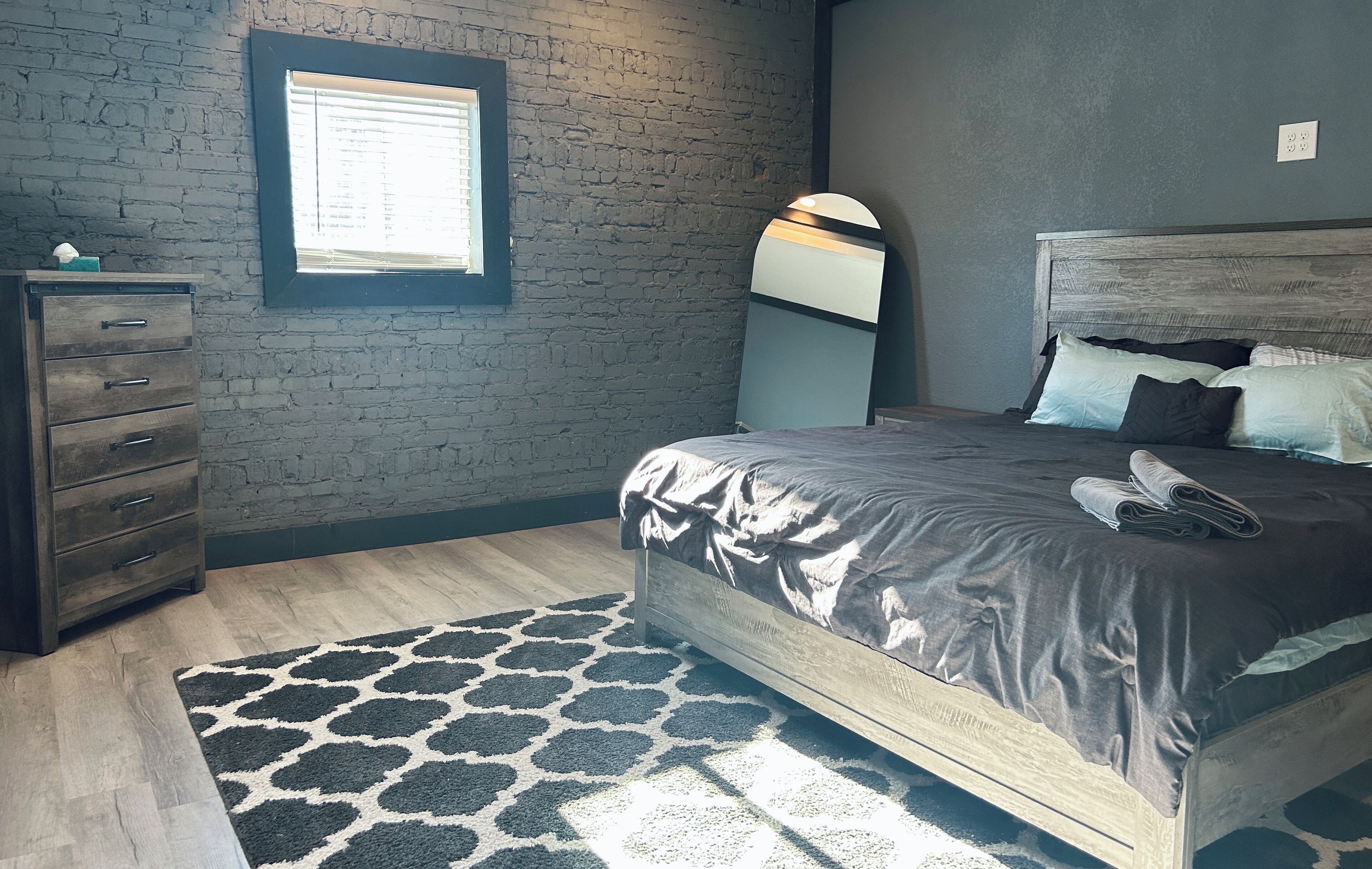 Une chambre à coucher avec un lit en bois, une commode, une fenêtre et un tapis à motifs.