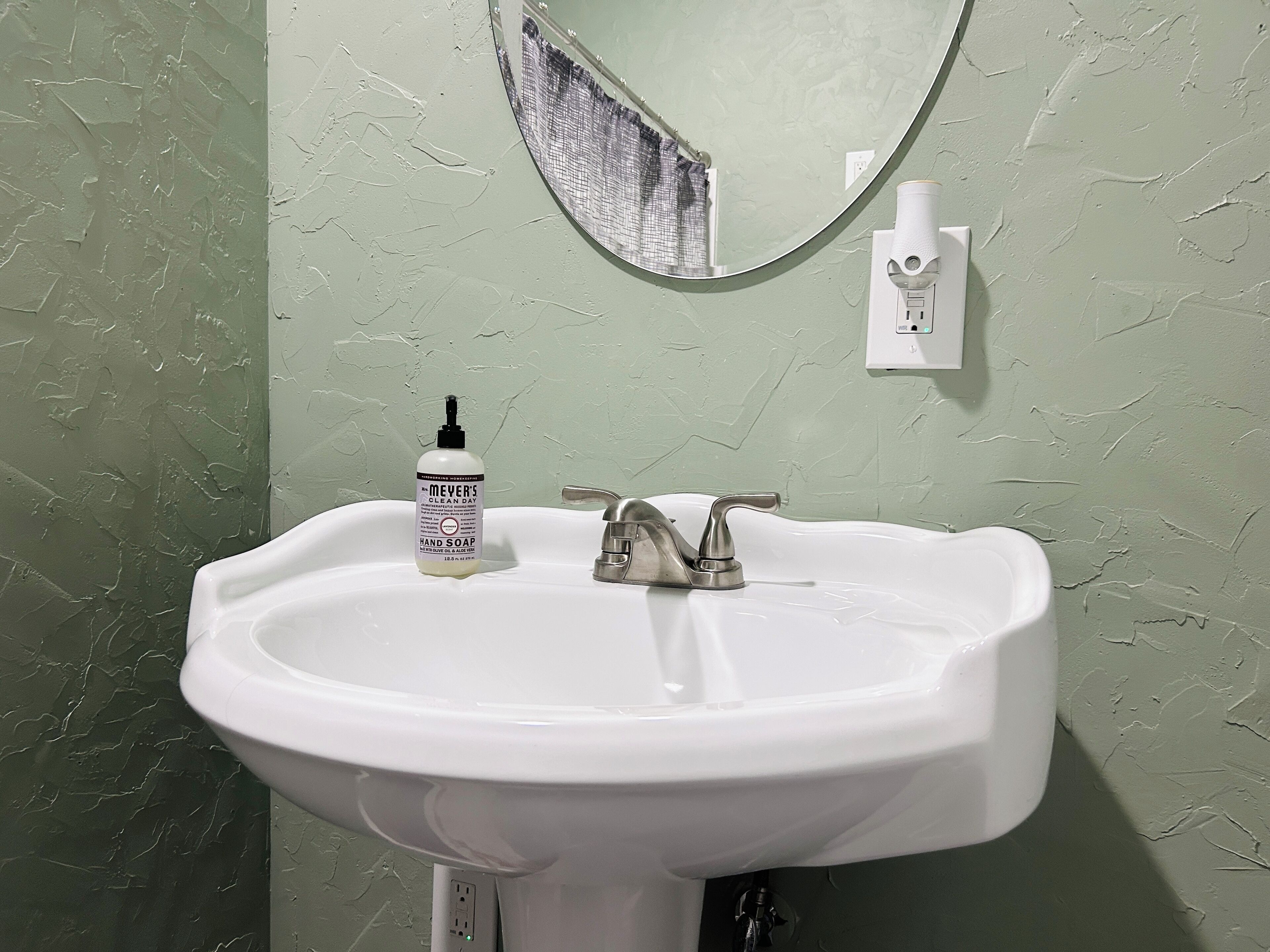 Ein Badezimmer mit einem weißen Waschbecken, einem Spiegel und einer Handseifenflasche.