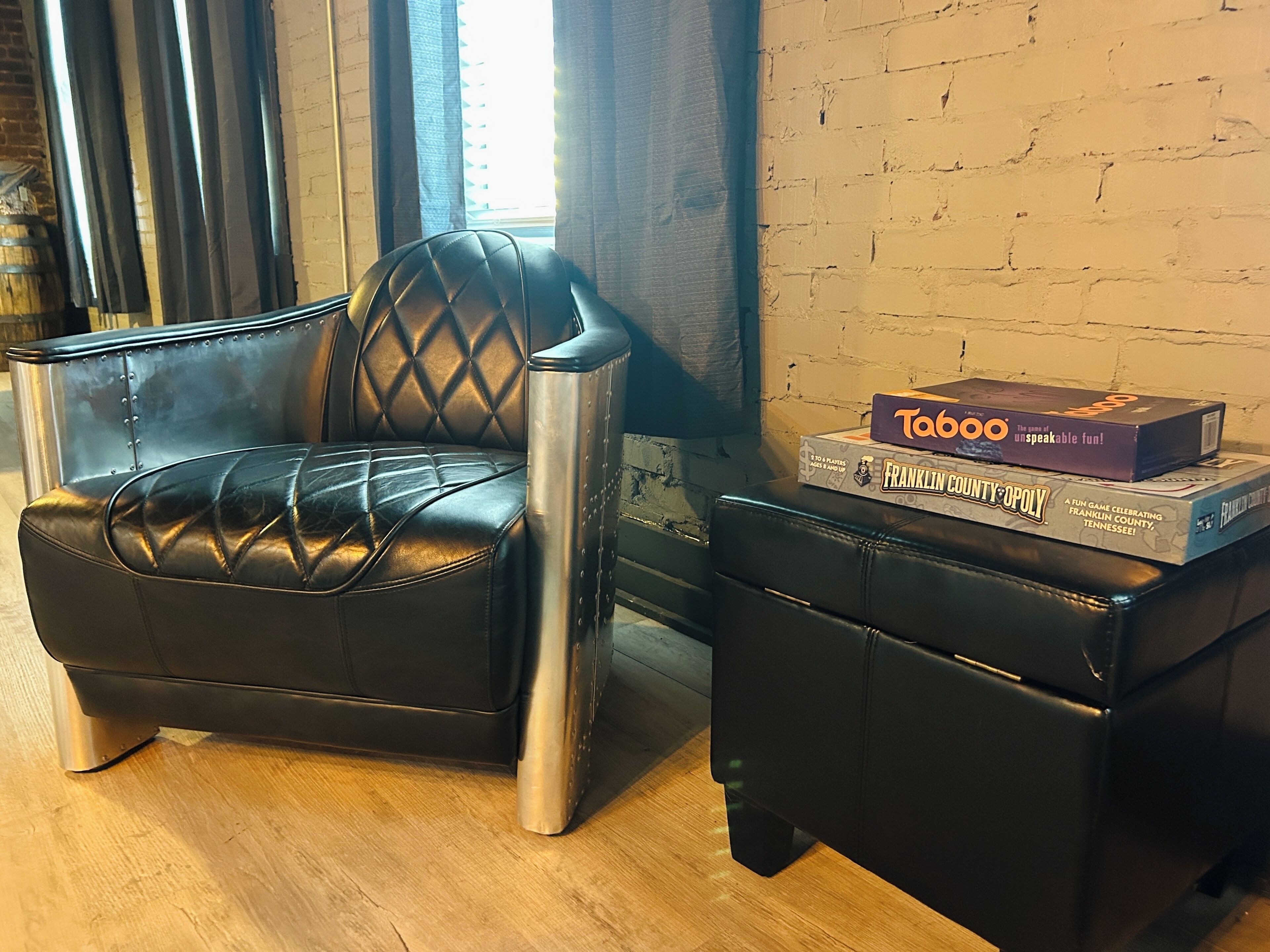 Un sillón y reposapiés de cuero negro con una pila de juegos de mesa encima.