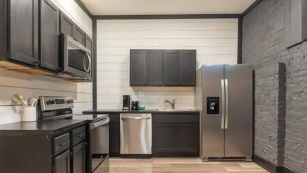Une cuisine moderne avec des meubles de couleur sombre, des appareils en acier inoxydable et un revêtement mural de couleur claire.