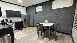 Une cuisine moderne avec des meubles de couleur sombre, un réfrigérateur en acier inoxydable et un coin repas comprenant une table et des chaises.