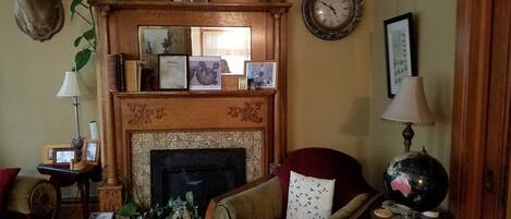 A cozy living room with a fireplace, a red armchair, a globe, and various framed pictures on the mantel.