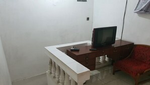 A room with a wooden desk, a television, a red chair, and a patterned tablecloth. - Hotel O Abang Homestay Syariah (Surabaya)