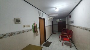 A hallway with a door, a wall-mounted light fixture, a wall-mounted fan, and a red chair. - Hotel O Abang Homestay Syariah (Surabaya)