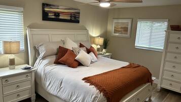 A neatly made bed with a white comforter and brown throw blanket, a ceiling fan, and artwork on the walls.