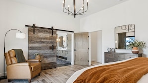 Un dormitorio moderno con una cama grande, un sillón de cuero, una puerta corredera que da a un baño y un candelabro.