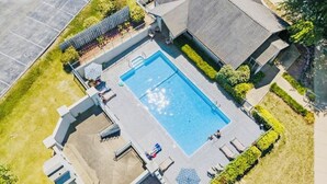 An aerial view of a residential property with a swimming pool, a covered patio, and a fenced garden area.