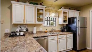 A kitchen with white cabinets, a stainless steel refrigerator, a granite countertop, and a coffee station.