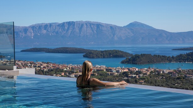 Eine Person im Schwimmbecken mit Blick auf eine Küstenstadt, im Hintergrund Berge.