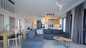 Ein modernes Wohnzimmer mit einem grauen Ecksofa, einem Holzessttisch mit Stühlen und einer Küche im Hintergrund.