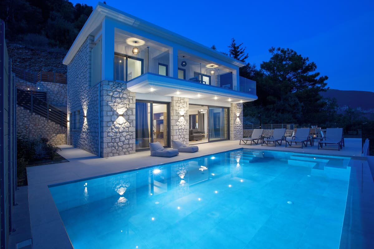 Una casa moderna de dos pisos con piscina, fachada de piedra y zona de estar al aire libre.