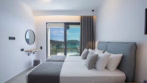 Ein modernes Hotelzimmer mit einem großen Bett, einem kleinen Tisch, einem Sessel und Blick ins Freie.