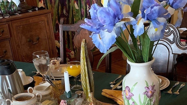 A dining table set with various dishes, a vase of flowers, and a decorative centerpiece. - Garden House Bed and Breakfast....Cozy 1895 Queen Anne Victorian, (HANNIBAL)