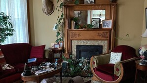A traditional living room with a fireplace, red armchairs, a coffee table, and a cat. - Garden House Bed and Breakfast....Cozy 1895 Queen Anne Victorian, (HANNIBAL)