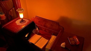 A dimly lit room with a wooden bench, a table with a book and a remote control, and a small lamp on a doily. - Garden House Bed and Breakfast....Cozy 1895 Queen Anne Victorian, (HANNIBAL)