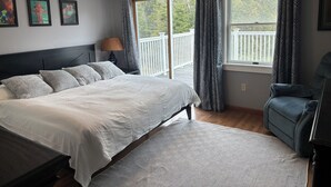 Et soveværelse med en stor seng, en stol, et vindue med gardiner og udsigt til en balkon.