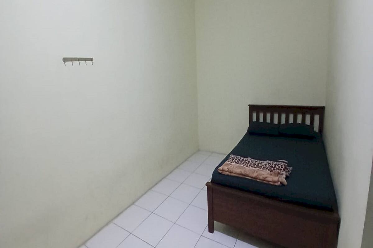 Ein kleines Zimmer mit einem Einzelbett, einem Holzkopfteil und einer grünen Bettdecke.
