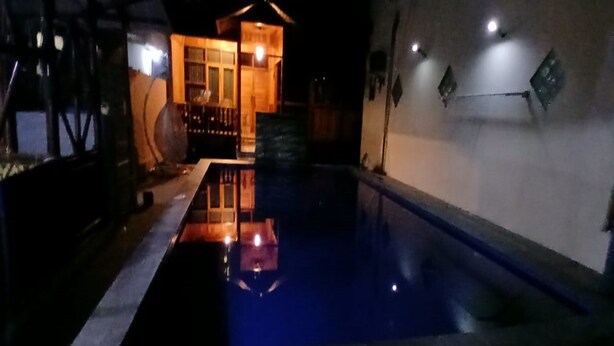 Una piscina con cubierta de madera y un edificio pequeño al fondo.