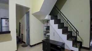 Una escalera con barandilla negra, pared blanca y una puerta que da a otra habitación.
