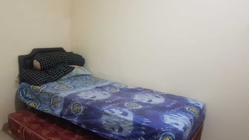 Una habitación pequeña con una cama individual, una colcha estampada y una maleta roja en el suelo.