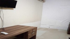 Quarto com uma secretária de madeira, televisão de tela plana na parede e piso revestido de azulejos.