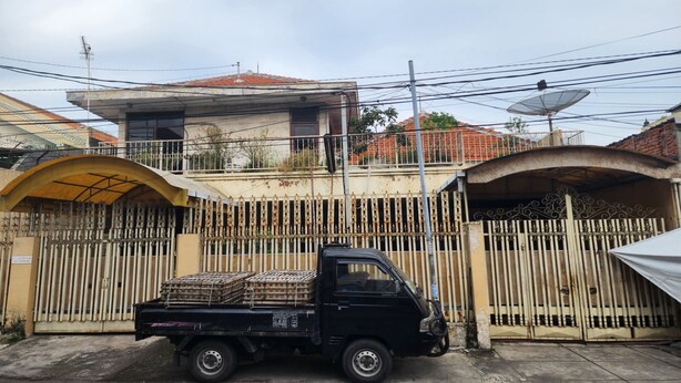 Uma caminhonete preta estacionada em frente a um condomínio com uma casa ao fundo.